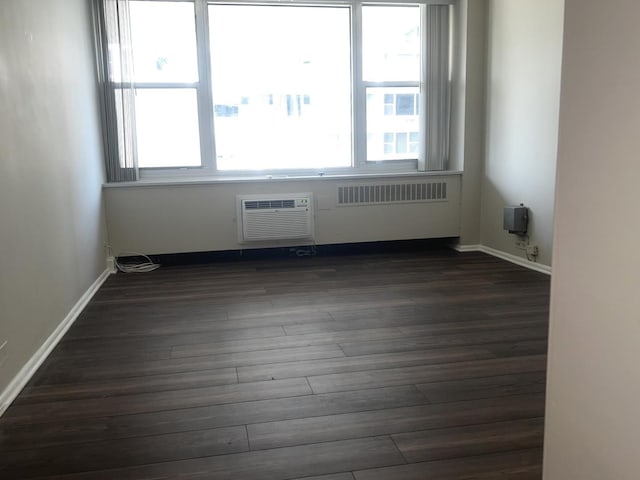 empty room with dark wood-type flooring, radiator, baseboards, and a wall mounted AC