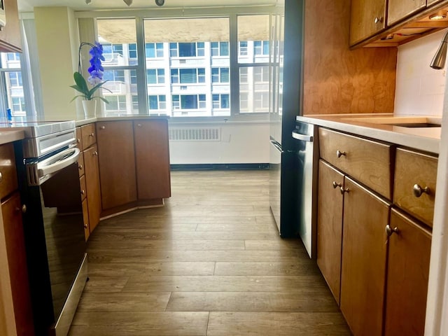 kitchen featuring stainless steel electric range oven, brown cabinetry, wood finished floors, a sink, and light countertops