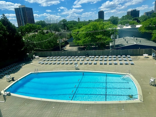 community pool with a view of city, a patio, and fence