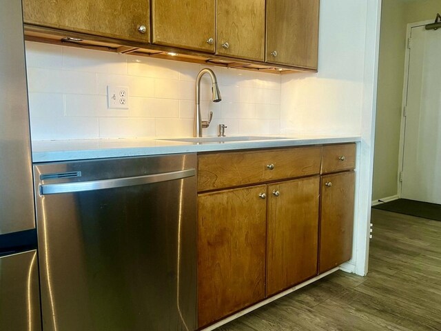 kitchen with stainless steel dishwasher, sink, wood-type flooring, and tasteful backsplash