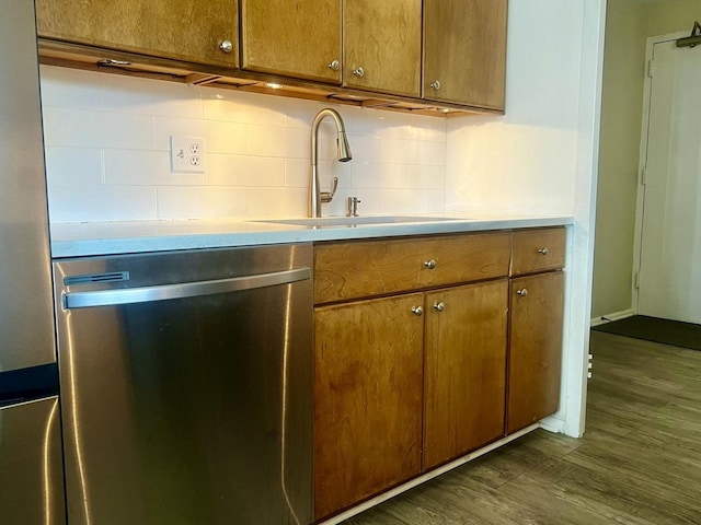 kitchen featuring backsplash, dark wood-type flooring, stainless steel dishwasher, brown cabinetry, and a sink