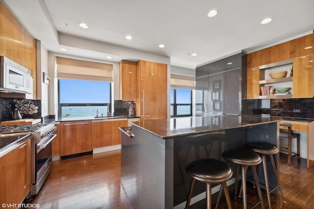 kitchen with dark stone counters, dark hardwood / wood-style flooring, tasteful backsplash, range with gas cooktop, and a center island