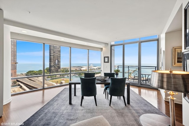 dining area with expansive windows, a water view, wood finished floors, and a wealth of natural light