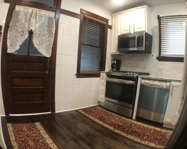 kitchen with hardwood / wood-style floors, stainless steel appliances, tile walls, backsplash, and white cabinetry