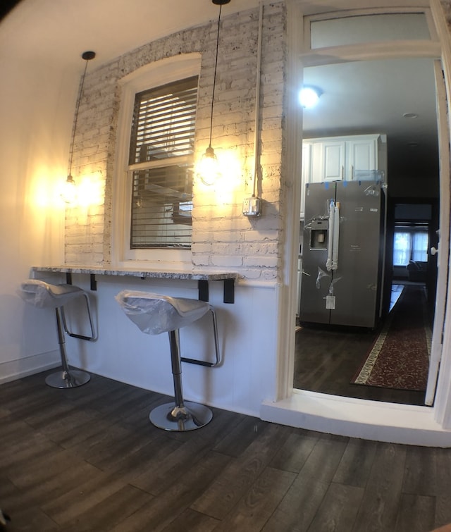 kitchen with stainless steel fridge with ice dispenser, dark hardwood / wood-style floors, light stone countertops, white cabinets, and a breakfast bar