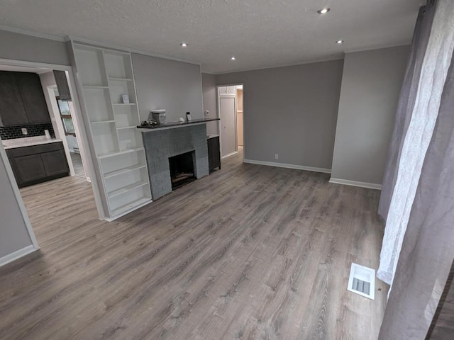 unfurnished living room featuring built in features, light wood-type flooring, and a textured ceiling