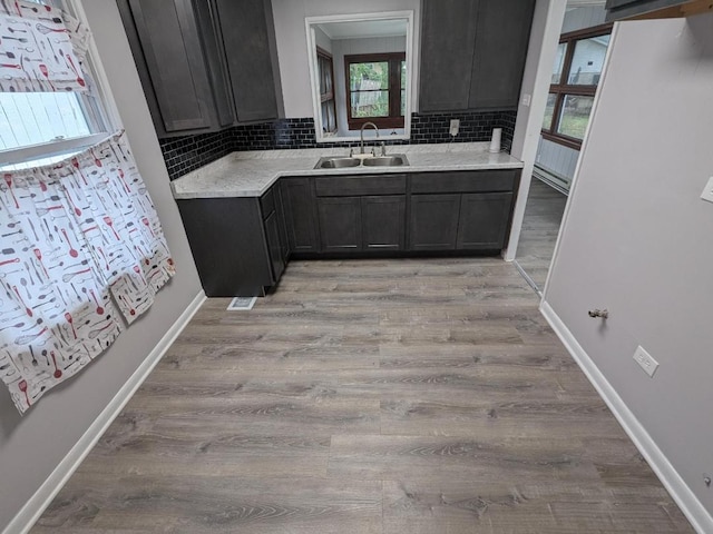 kitchen with light stone counters, tasteful backsplash, light hardwood / wood-style flooring, and sink