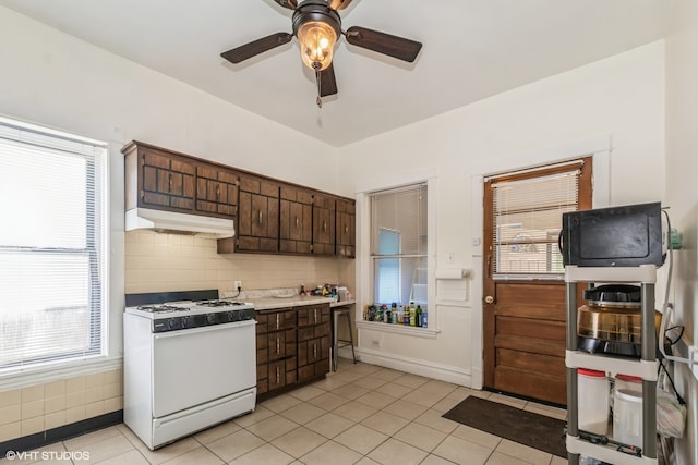 kitchen with a healthy amount of sunlight, ceiling fan, white gas stove, and light tile flooring