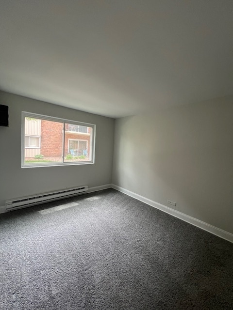 carpeted empty room featuring a baseboard heating unit