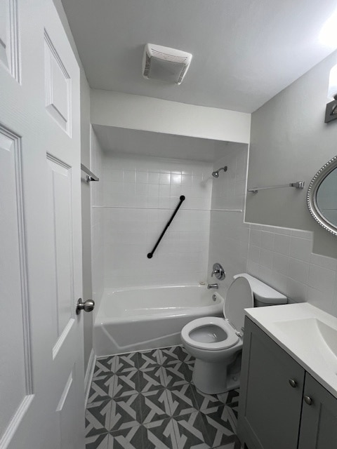 full bathroom featuring tile walls, toilet, tile flooring, tiled shower / bath, and vanity