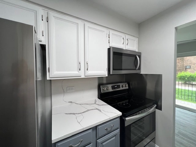 kitchen with plenty of natural light, hardwood / wood-style floors, white cabinets, and appliances with stainless steel finishes