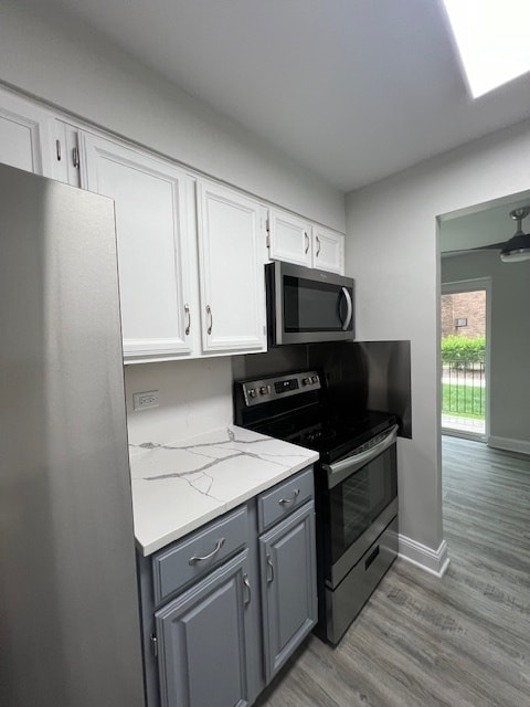 kitchen with light hardwood / wood-style flooring, stainless steel appliances, gray cabinetry, white cabinetry, and light stone countertops