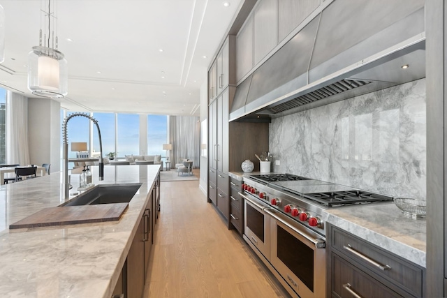 kitchen with light stone countertops, hanging light fixtures, light hardwood / wood-style flooring, range with two ovens, and custom exhaust hood