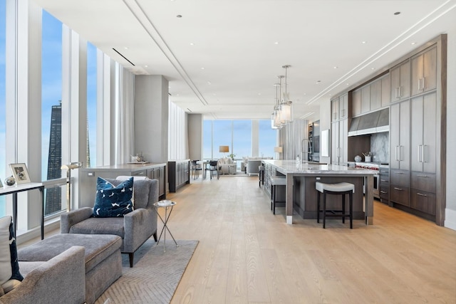 kitchen featuring a large island, hanging light fixtures, a wall of windows, light hardwood / wood-style flooring, and a kitchen bar