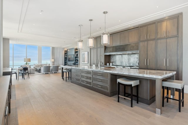 kitchen with a kitchen bar, light wood-type flooring, expansive windows, a large island with sink, and pendant lighting