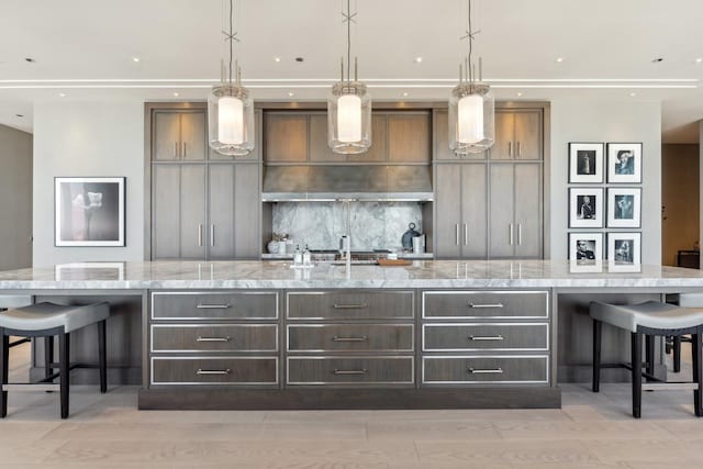 kitchen featuring a large island with sink, light stone countertops, and hanging light fixtures