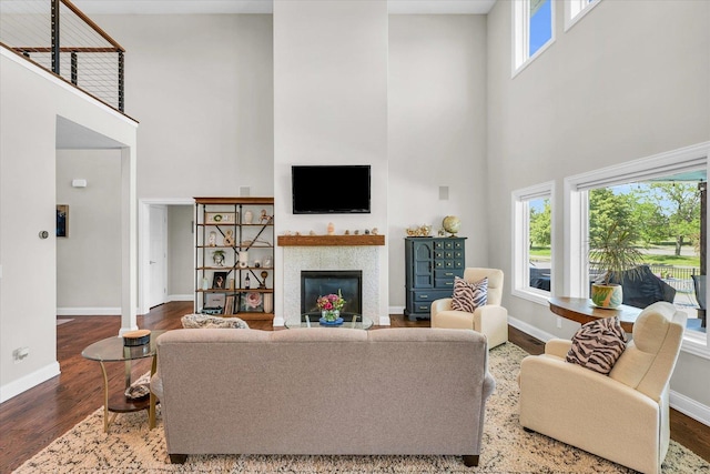 living room with a tiled fireplace, a towering ceiling, a healthy amount of sunlight, and hardwood / wood-style flooring