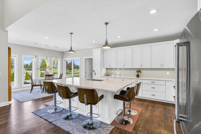 kitchen with high quality fridge, dark hardwood / wood-style floors, a kitchen island with sink, and white cabinets