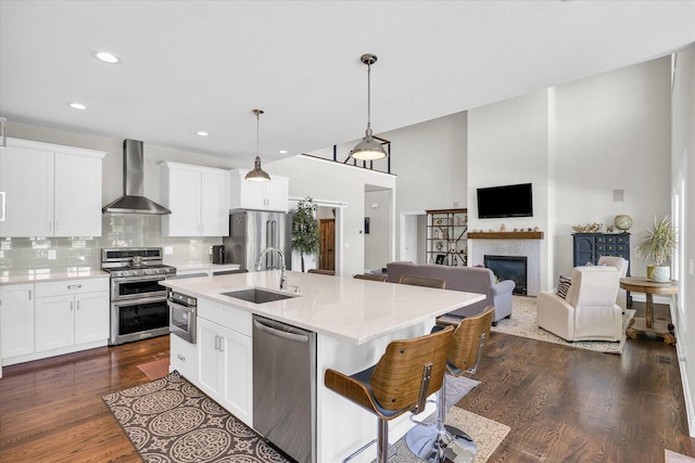 kitchen with sink, white cabinetry, decorative light fixtures, appliances with stainless steel finishes, and wall chimney range hood