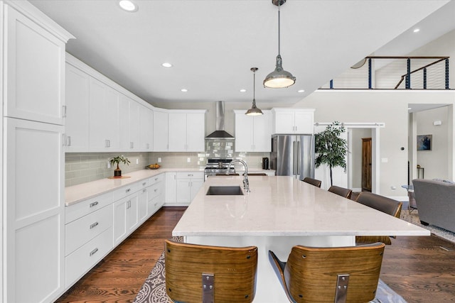 kitchen with sink, white cabinetry, hanging light fixtures, appliances with stainless steel finishes, and wall chimney range hood