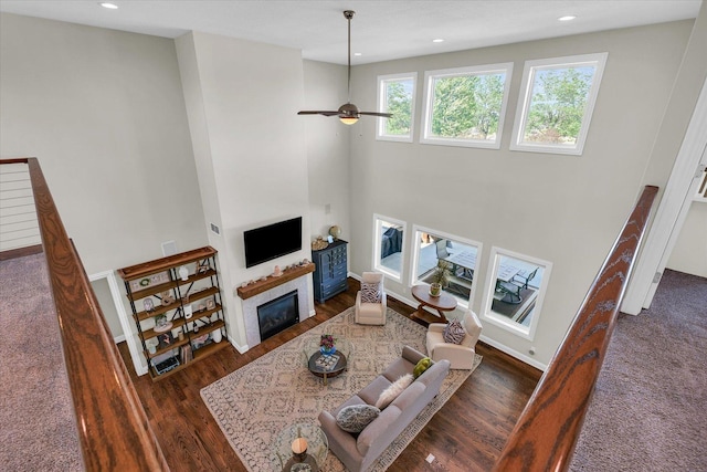 living room featuring dark wood-type flooring, ceiling fan, and a high ceiling