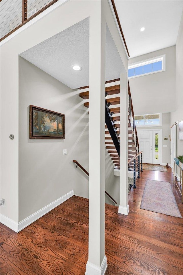 staircase with hardwood / wood-style floors, a towering ceiling, and a textured ceiling