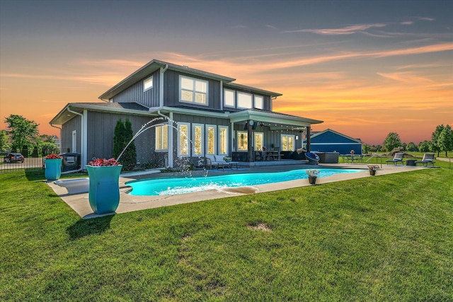 back house at dusk featuring a patio, pool water feature, and a lawn