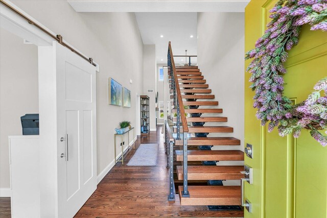 staircase featuring a barn door, a towering ceiling, and hardwood / wood-style floors