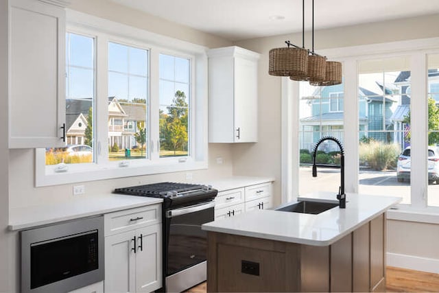 kitchen with appliances with stainless steel finishes, white cabinetry, a kitchen island with sink, and sink