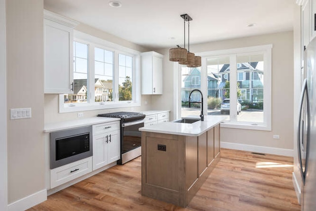 kitchen with white cabinets, appliances with stainless steel finishes, a center island with sink, and sink