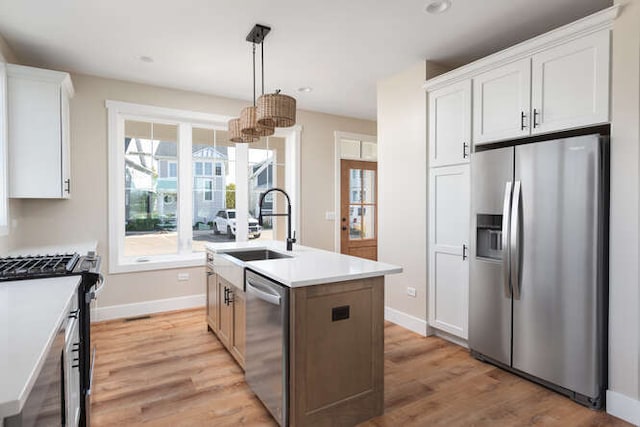 kitchen featuring stainless steel appliances, sink, decorative light fixtures, a center island with sink, and white cabinets