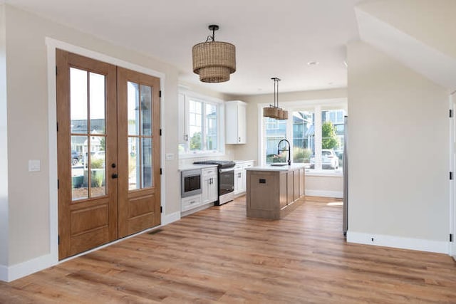 kitchen featuring french doors, a kitchen island with sink, pendant lighting, light hardwood / wood-style flooring, and white cabinets