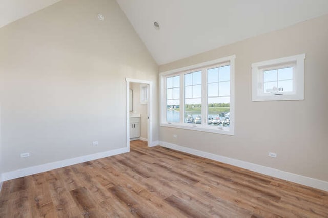 unfurnished bedroom featuring ensuite bath, light hardwood / wood-style floors, high vaulted ceiling, and multiple windows