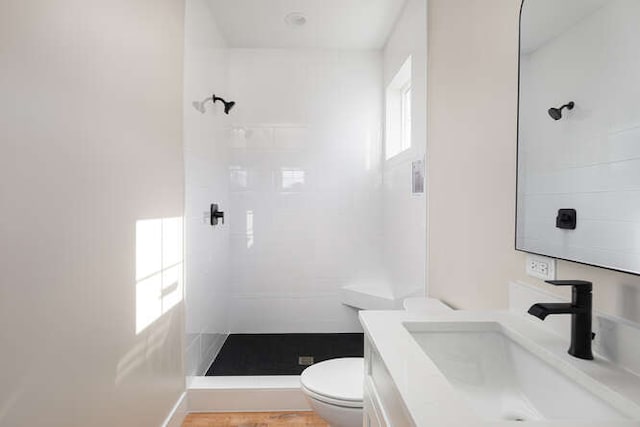 bathroom with a tile shower, vanity, and toilet