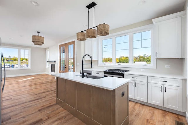 kitchen with sink, light hardwood / wood-style flooring, decorative light fixtures, a center island with sink, and white cabinets