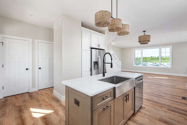 kitchen with light wood-type flooring, stainless steel appliances, sink, hanging light fixtures, and an island with sink