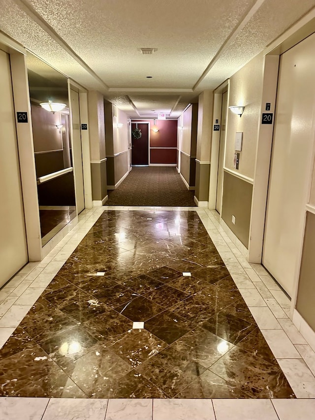 corridor with a textured ceiling, elevator, and light tile floors