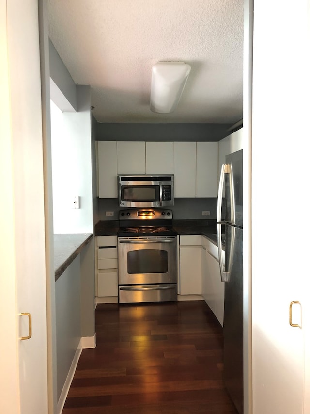 kitchen featuring appliances with stainless steel finishes, white cabinetry, a textured ceiling, and dark wood-type flooring