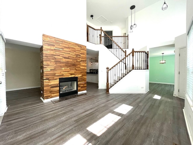 unfurnished living room featuring a fireplace, a towering ceiling, and dark wood-type flooring