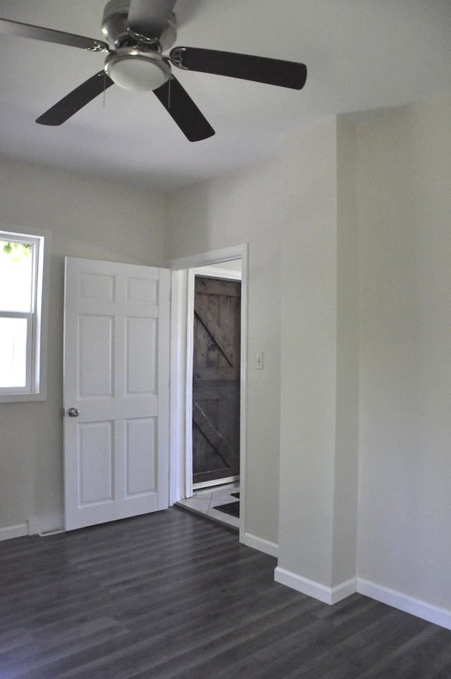 unfurnished room with ceiling fan, a barn door, and dark hardwood / wood-style flooring