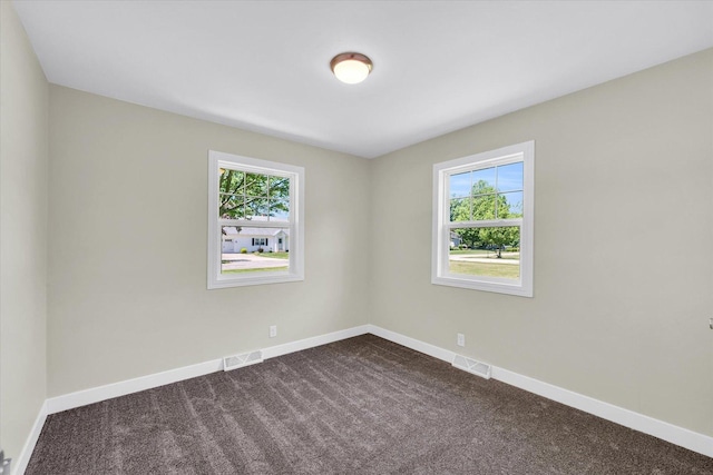 spare room with a healthy amount of sunlight, visible vents, dark carpet, and baseboards