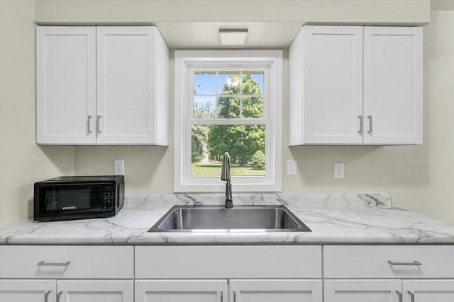 kitchen featuring light stone counters, a sink, and white cabinetry