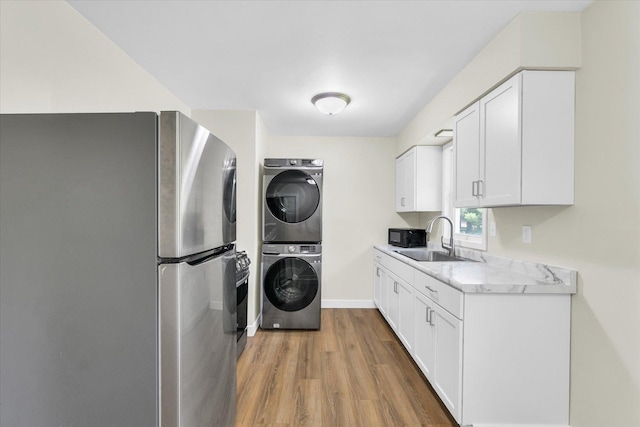 laundry area with stacked washer / dryer, a sink, wood finished floors, laundry area, and baseboards