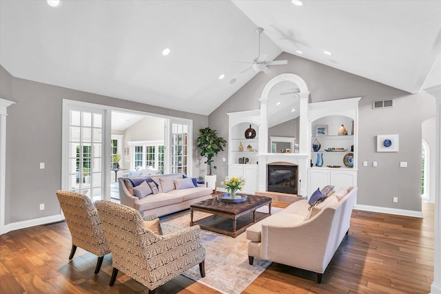 living room featuring baseboards, visible vents, built in features, a glass covered fireplace, and hardwood / wood-style floors