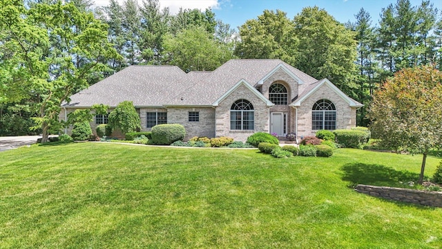 view of front of property with a front yard, roof with shingles, and brick siding