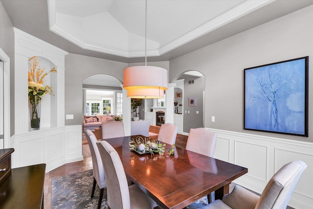 dining room featuring visible vents, dark tile patterned flooring, lofted ceiling, wainscoting, and a decorative wall