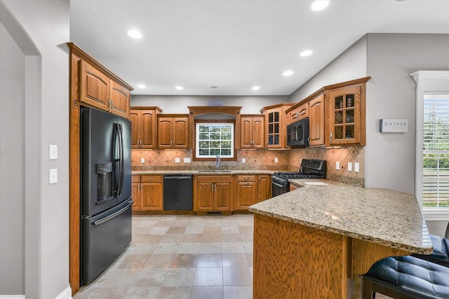 kitchen with brown cabinetry, glass insert cabinets, a peninsula, black appliances, and a sink