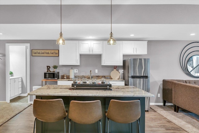 kitchen with appliances with stainless steel finishes, white cabinets, light wood finished floors, and light stone countertops