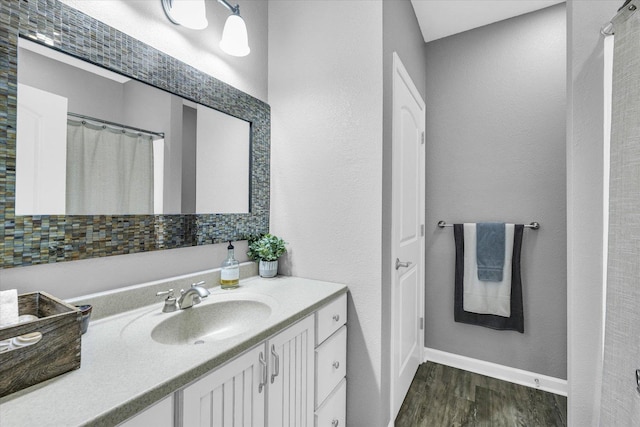 bathroom featuring a textured wall, vanity, baseboards, and wood finished floors