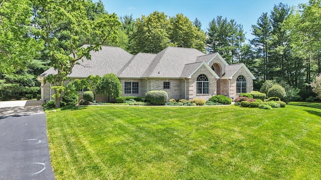 view of front of house with a front lawn, roof with shingles, and aphalt driveway